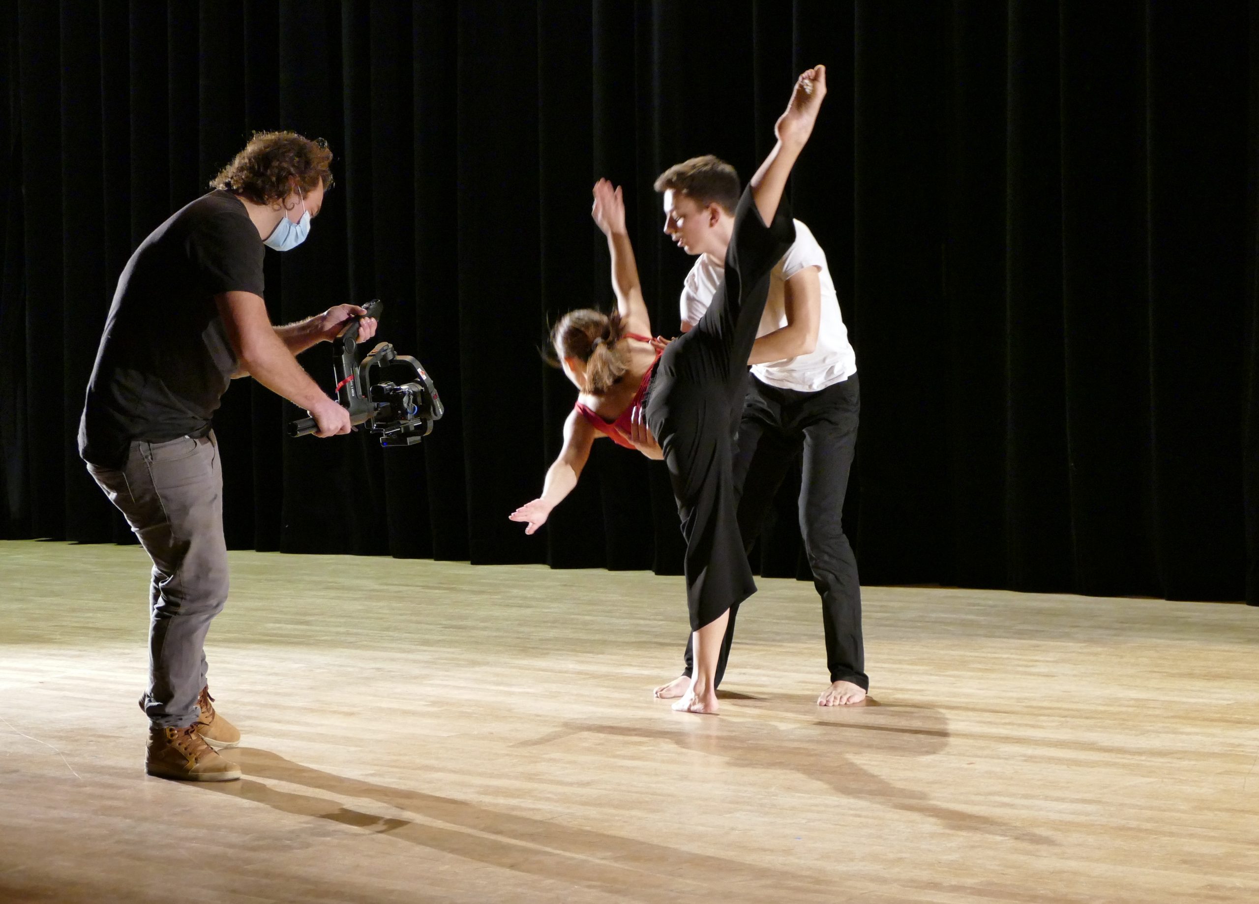 "Unis par la danse", tournage du documentaire au conservatoire de Boulogne-Billancourt - danseur et danseuse se tenant la main pendant la chorégraphie sur scène, avec un caméraman à gauche